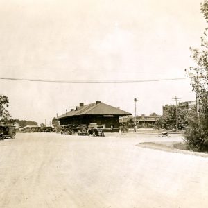 Street with storefronts, parked cars, and train station