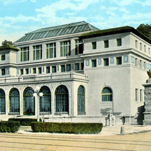 Symmetrical three-story building with large arched windows on the ground level and street