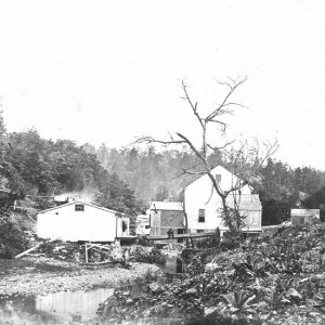 Wooden buildings positioned alongside steam with trees in the background