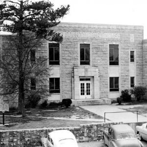 Two-story brick building with stone wall and parked cars in front