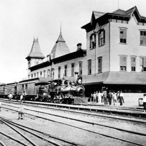 Steam locomotive with cars parked at a two-story train station