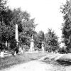 Rows of tall monuments and trees with cemetery road