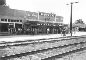 Crowd of people standing outside "Dante's" department store, with railroad tracks in foreground