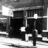 Four men stand by entrance brick gas station with pump and "Ford authorized service" sign