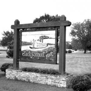 Wooden sign "Jacksonport State Park" with riverboat carving in field, gazebo in background