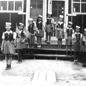 Asian-American girls pose in v-shape on steps in matching outfits and hats, holding flags