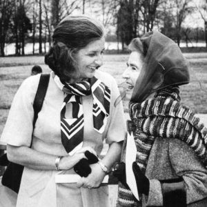 Two white women with scarves chat and laugh in park by river