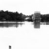 Lake with bridge and various brick buildings in background along wooded shoreline