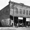 Two story brick building "Alma Drug Co." with onlookers, horse and carriage, faded "Ringling Bros" wall print