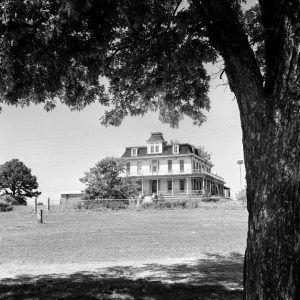 Fenced-in three-story Victorian home with wrap around porch and balcony on grassy hill