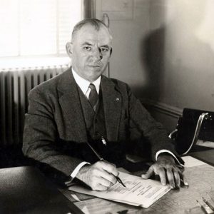 Portrait white man in suit at office desk posing signing document