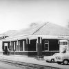 brick building with angled spanish tile roof and "Bald Knob" sign parked vehicles by railroad tracks