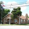 Single-story building with stone walls sign flagpole and tree in front