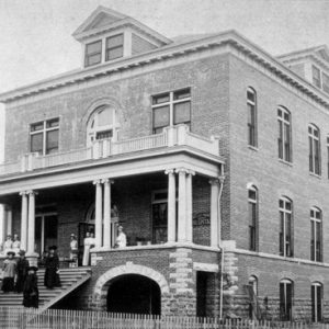 three story brick building with people on front steps and porch