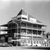 Multistory building with storefronts on first floor with signs reading "cafe" and "motel" and cars parked in front