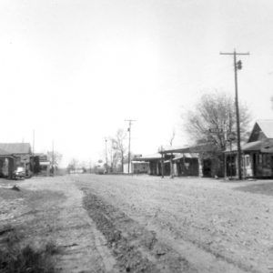 Dirt road lined with buildings and trees in the background