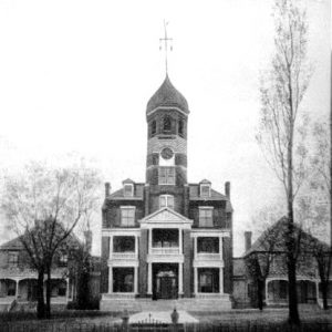 Multistory building with porches balconies and central clock tower between two smaller neighboring buildings with an iron fence