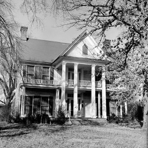 Two story wood frame home with two story porch balcony two chimneys yard and trees