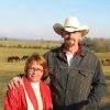 white woman and white man in cowboy hat in pasture with horses in background