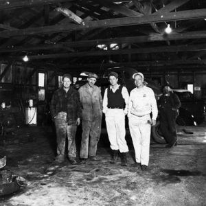 men posing in garage with cars in background and foreground