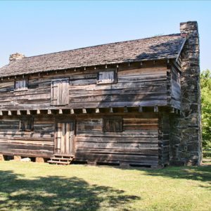 two-story wooden building with stone chimneys on either side and central doors on both stories