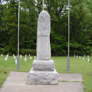 rough hewn stone monument with names engraved  standing before three flagpoles amid larger cemetery