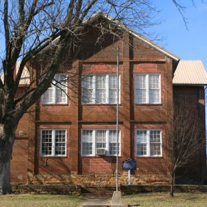 two-story brick building with flagpole and tree