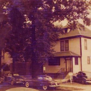 Three story home with front and side steps and parked cars trees