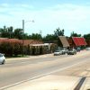 Traffic driving past single-story storefronts on two-lane street