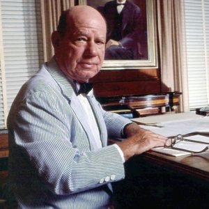 Portrait of white man in seersucker suit, bow tie, seated at writing desk