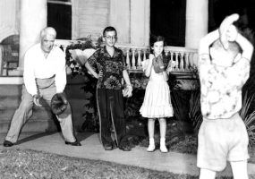White man, two white boys, and white girl play catch with ball and gloves by front porch