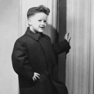 Portrait young boy posing smiling in matching shoes slacks long jacket foot hand on column