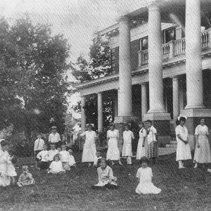 Group of women and children outside two-story house with four columns and balcony