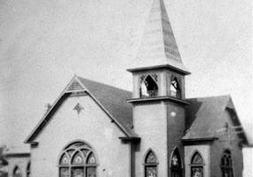Single-story church building with arched stained glass windows and bell tower