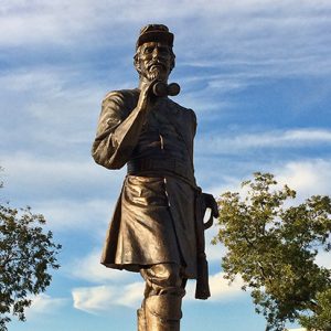 Statue of white man in military uniform with binoculars on stone  pedestal