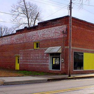 Brick storefront on street with faded words "Clem's Bottling Works" on its side