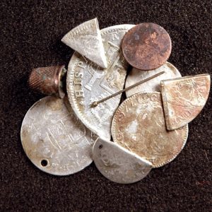 Stack of coins and coin pieces with thimble and metal pin