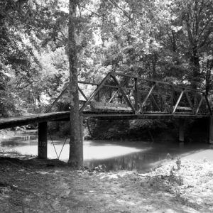 Narrow steel bridge with wooden slats over  wooded creek