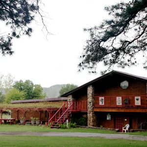 two-story wooden building with stone pillars and grape arbor alongside it