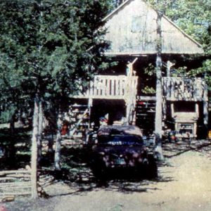 Parked cars outside a multistory cabin with a balcony and trees