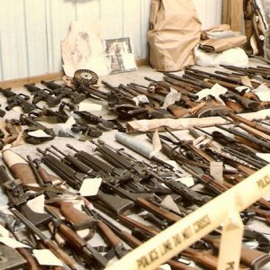 Rows of guns laid out on the floor with paper tags surrounded by yellow police tape