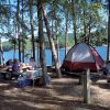 three white people at picnic table near tent at the lakeside