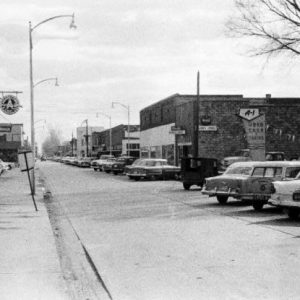 Brick storefront buildings with signs light posts parked vehicles "A-1 Used Cars and trucks" sign with winter trees