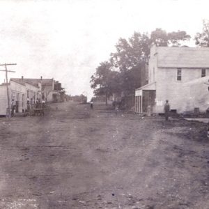 Town street with dirt road, wood framed buildings, brick bank, pedestrians