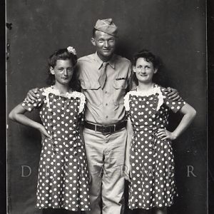 Portrait white male soldier with arms around two shorter white women matching polka dot dresses