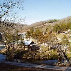 Hillside village along river with dam suspension bridge wood frame buildings gravel roads and trees