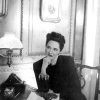 White woman wearing pearls sitting at her desk