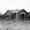 Wood shingled home by trees with flag pole scrubby yard and wall sign saying "Winslow American"