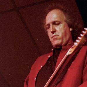 White man in red shirt playing electric guitar