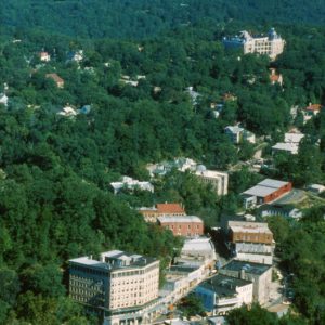 City aerial view with forking, winding roads, hotels, businesses, homes among forest, mountains in distance